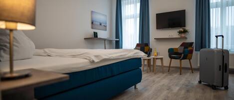 A hotel room with a bed, a desk, a chair, a TV, and a suitcase.