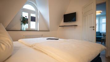 A bedroom with a large bed, a TV mounted on the wall, and a window with a view of the outside.