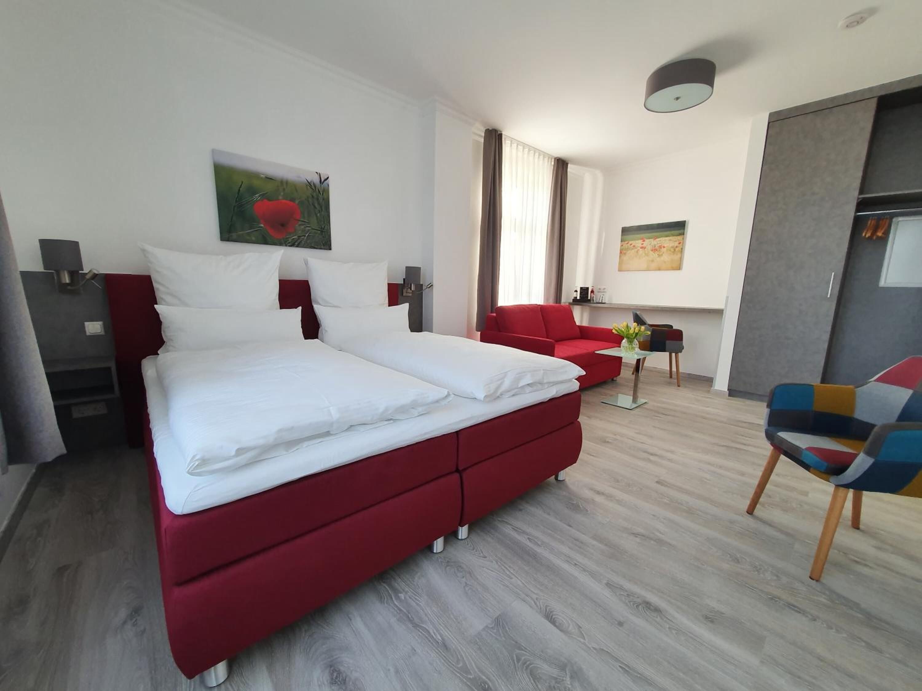 A modern hotel room with a large bed, red sofa, and a small table with flowers.