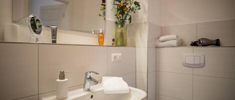 Un baño con lavamanos, espejo, artículos de aseo y un florero con flores.