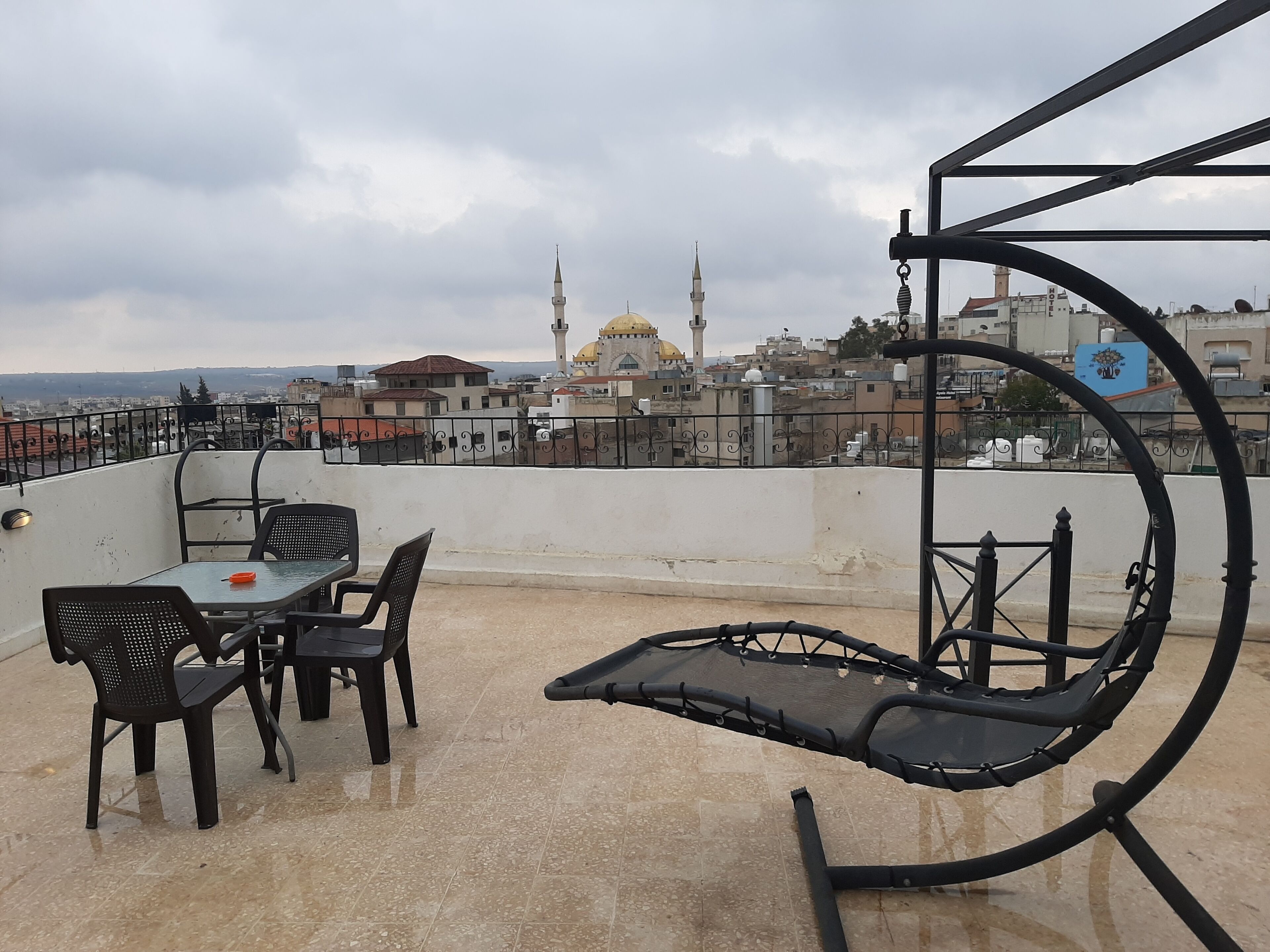 Una terraza en la azotea con mesa y sillas, un sillón colgante y vistas a una mezquita con dos alminares y una cúpula.