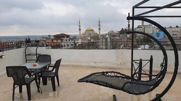 Una terraza en la azotea con mesa y sillas, un sillón colgante y vistas a una mezquita con dos alminares y una cúpula.