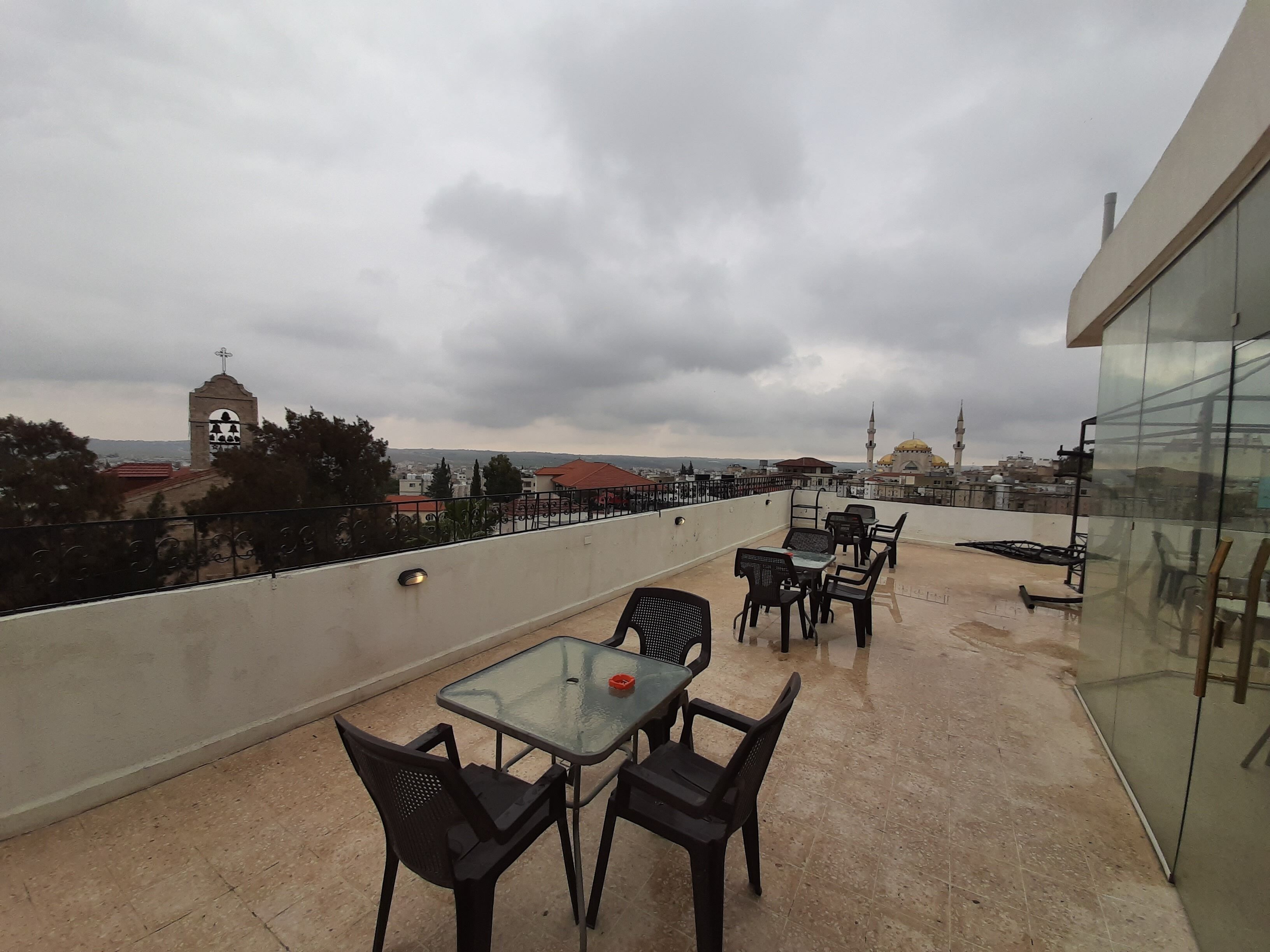 Terraço no telhado com mesa e cadeiras de vidro, com vista para um horizonte urbano com edifícios e uma mesquita.