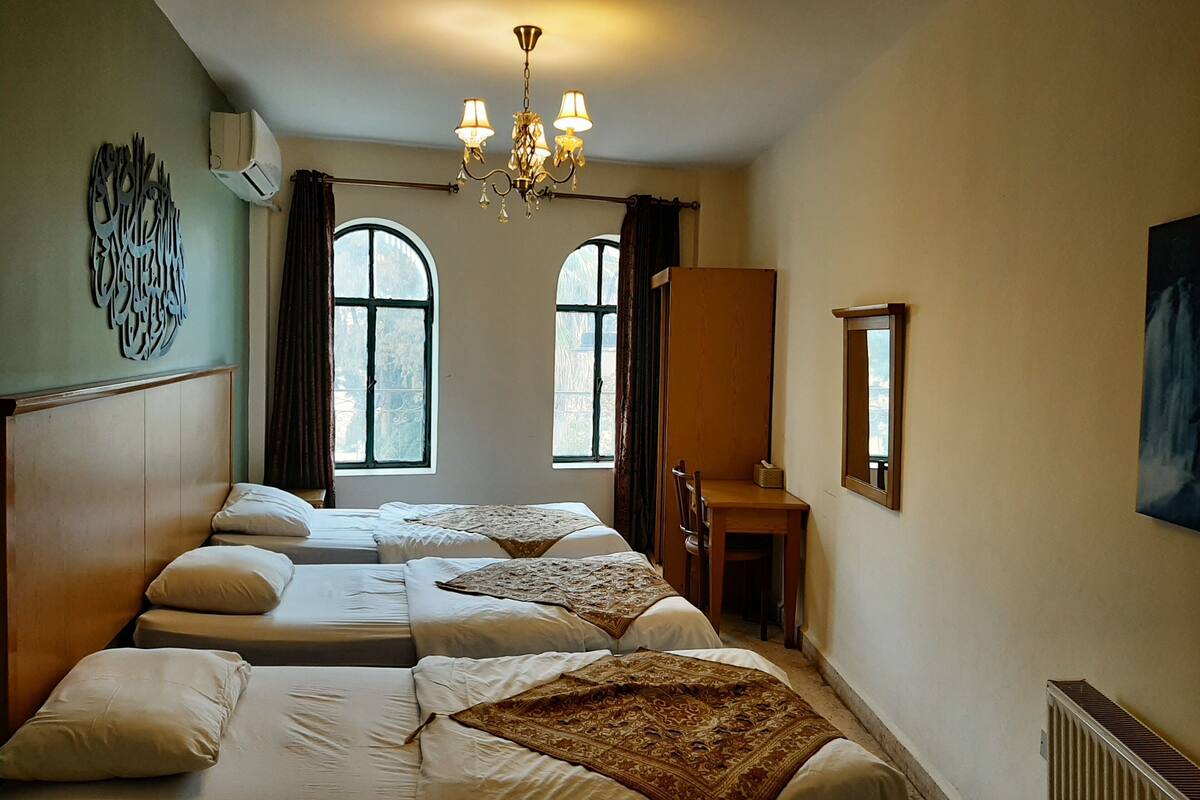 A hotel room with two beds, a wooden desk, a chair, a mirror, and a chandelier.