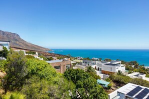 A coastal residential area with modern houses, a mountain in the background, and a clear view of the ocean.