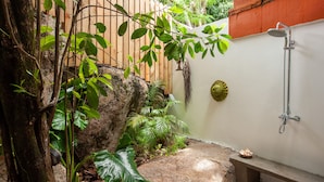 A small, enclosed outdoor shower area with a wooden fence, a stone bench, and lush greenery. - Free Wifi + Outdoor shower at La Pointe Beach Huts (Praslin)