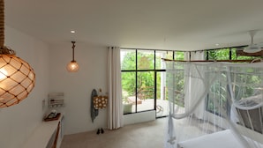 A room with a large window, a bed with a canopy, a hanging light fixture, and a small table with a basket. - Free Wifi + Outdoor shower at La Pointe Beach Huts (Praslin)