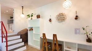 A modern interior with a staircase, wooden chairs, a white shelf unit, and decorative wall hangings. - Free Wifi + Outdoor shower at La Pointe Beach Huts (Praslin)