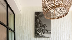 A modern living room with a white sofa, tropical-themed cushions, a wooden coffee table, and a woven pendant light. - Free Wifi + Outdoor shower at La Pointe Beach Huts (Praslin)