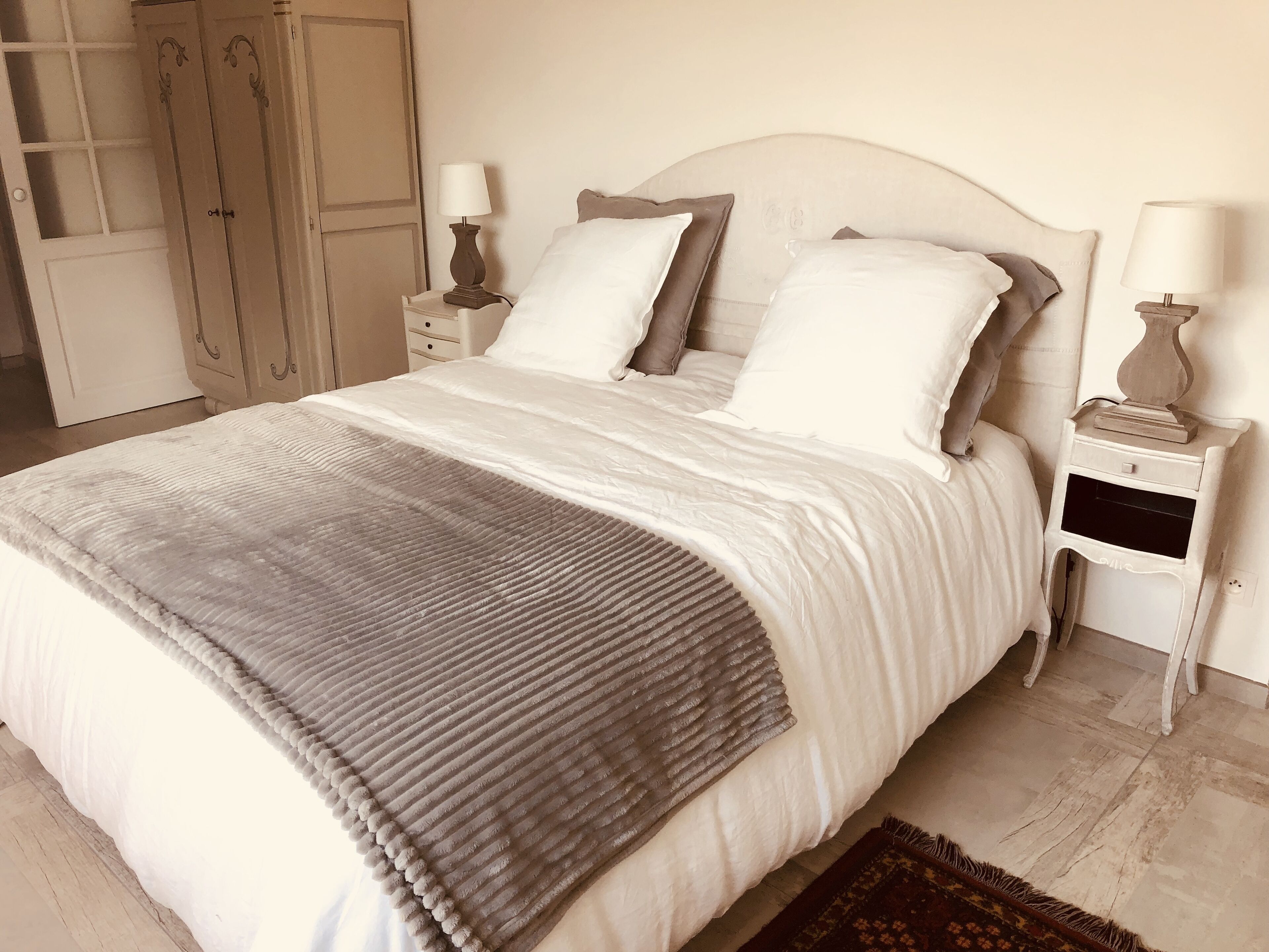 A neatly made bed with a grey throw blanket, white bedding, and two bedside tables with lamps.