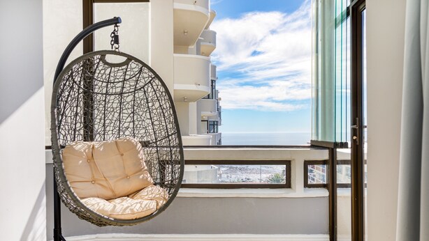 Un balcón con una hamaca colgante, vista al mar y un edificio con balcones.