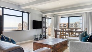 Un salón espacioso con un gran ventanal, un televisor de pantalla plana, una mesa de centro de madera y un balcón con comedor.