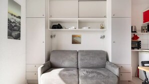 A compact living space with a grey sofa, white cabinets, and a small kitchen area with a toaster.