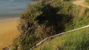A coastal landscape with a sandy beach, grassy cliffs, and a clear view of the sea.