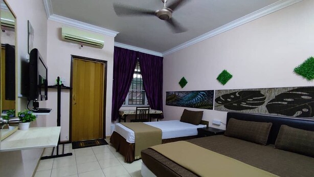 A hotel room with a bed, a desk, a chair, a television, and a window with purple curtains. - Hotel Sri Bahau (Bahau)