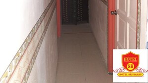 A narrow hallway with a red door on the right, a white door at the end, and a sign for 'HOTEL SRI BAHAU' at the bottom. - Hotel Sri Bahau (Bahau)