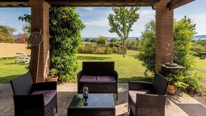 A covered patio with wicker furniture, a dartboard, and a view of a lush garden and distant landscape. - Cosy apartment in villa for 6 people with WIFI, pool, TV, terrace and pets allowed (Lake Bolsena)