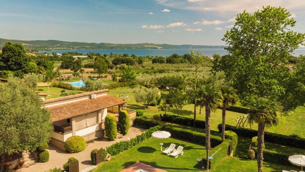 A pool area with a view of a lake, surrounded by well-maintained lawns and trees. - Cosy apartment in villa for 6 people with WIFI, pool, TV, terrace and pets allowed (Lake Bolsena)