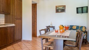A dining area with a wooden table, chairs, and a sofa. There is a painting on the wall and a television mounted above the sofa. - Cosy apartment in villa for 6 people with WIFI, pool, TV, terrace and pets allowed (Lake Bolsena)