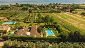 An aerial view of a property with a swimming pool, multiple buildings, and a large body of water in the background. - Cosy apartment in villa for 6 people with WIFI, pool, TV, terrace and pets allowed (Lake Bolsena)