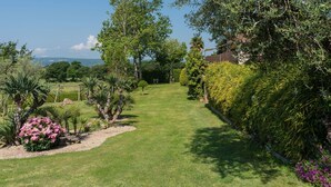 A well-maintained garden with a variety of trees and shrubs, a clear pathway, and a view of distant hills. - Cosy apartment in villa for 6 people with WIFI, pool, TV, terrace and pets allowed (Lake Bolsena)
