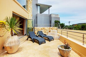 A modern outdoor seating area with two lounge chairs, a large potted plant, and a stone wall. - Backup-Powered Spacious 300sqm Condo on Bakoven Beach with Private Outdoor Pool (Cape Town)