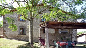 Un bâtiment rustique en pierre, agrémenté d’une pergola en bois et d’un espace extérieur aménagé pour s’asseoir.
