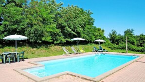 Une piscine rectangulaire entourée d’une terrasse dallée, de chaises longues vertes et de parasols.