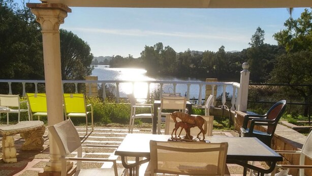 Eine Terrassensitzgruppe mit Tischen und Stühlen mit Blick auf ein Gewässer und Bäume.