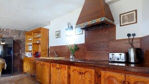 Eine Küche mit Holzausstattung, einer Steinwand, einem eingebauten Herd und einer Pendelleuchte.