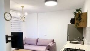 A compact living space with a sofa, a small table, a kitchen area with a stove, and a ceiling light fixture. - next to Soroka and BGU (Beer sheva)