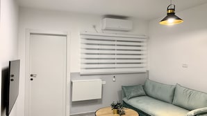 A modern living room with a sofa, a small round table with a plant, a TV, a ceiling light, and an air conditioning unit. - next to Soroka and BGU (Beer sheva)