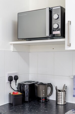 A kitchen with a microwave on a shelf, a toaster, a coffee maker, and a utensil holder on the counter. - SAV Wembley Studios (Wembley)