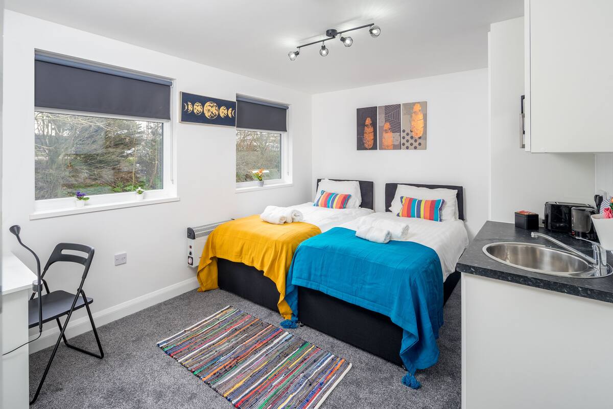 A modern bedroom with a bed, a desk, and a window with blinds.