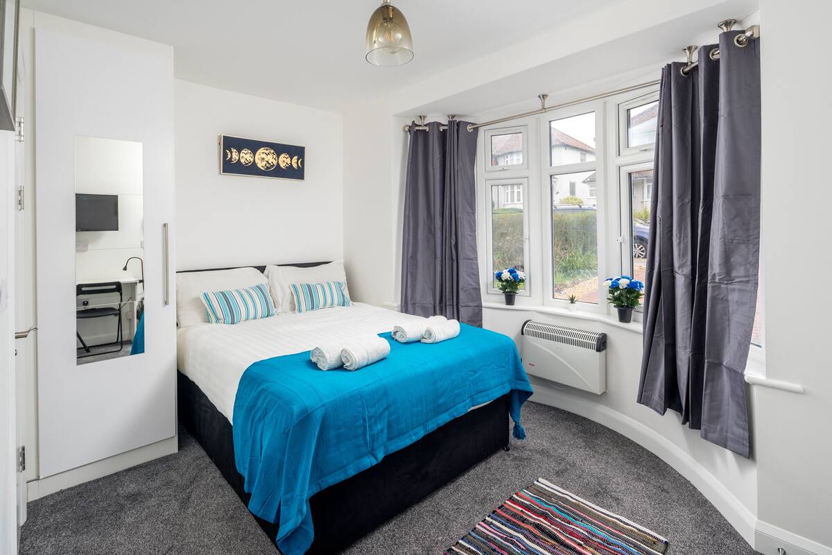 A bedroom with a bed, a window with curtains, a radiator, and a small potted plant.