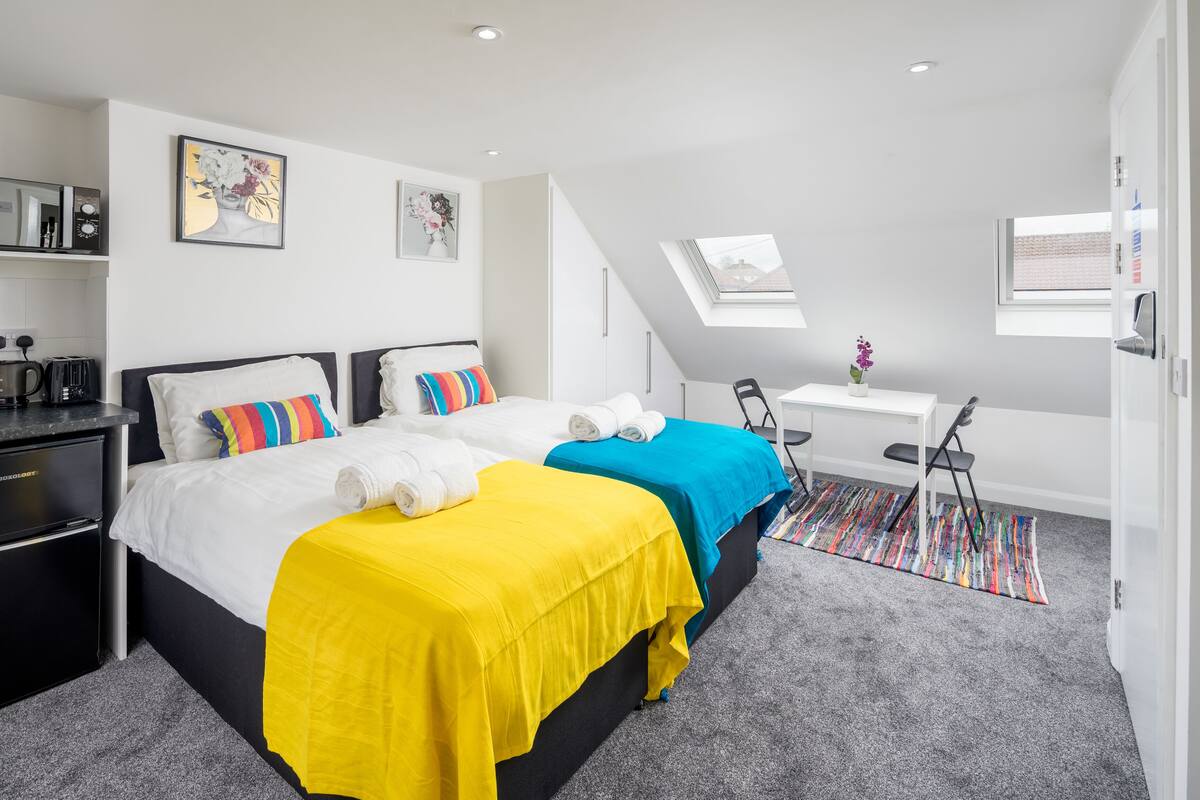 A modern hotel room with two beds, a desk, and a skylight.