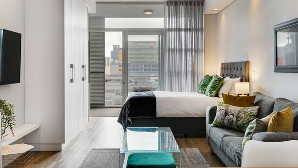 Une chambre d’hôtel moderne équipée d’un lit, d’un canapé, d’une télévision et d’un balcon offrant une vue sur la ville.