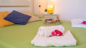 Una cama bien tendida con almohadas, una mesita de noche con una lámpara y una bandeja de aperitivos.