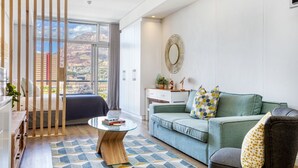 En moderne stue med sofa, sofabord og udsigt til et bjerrelandskab gennem store vinduer.