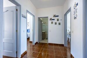 A hallway with white walls, brown tiled flooring, and a door leading to a bathroom.