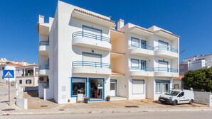 A multi-story building with balconies, a visible ground-floor shop, and a parked car. - CoolHouses Algarve Luz | Delicia do Sol (Luz)
