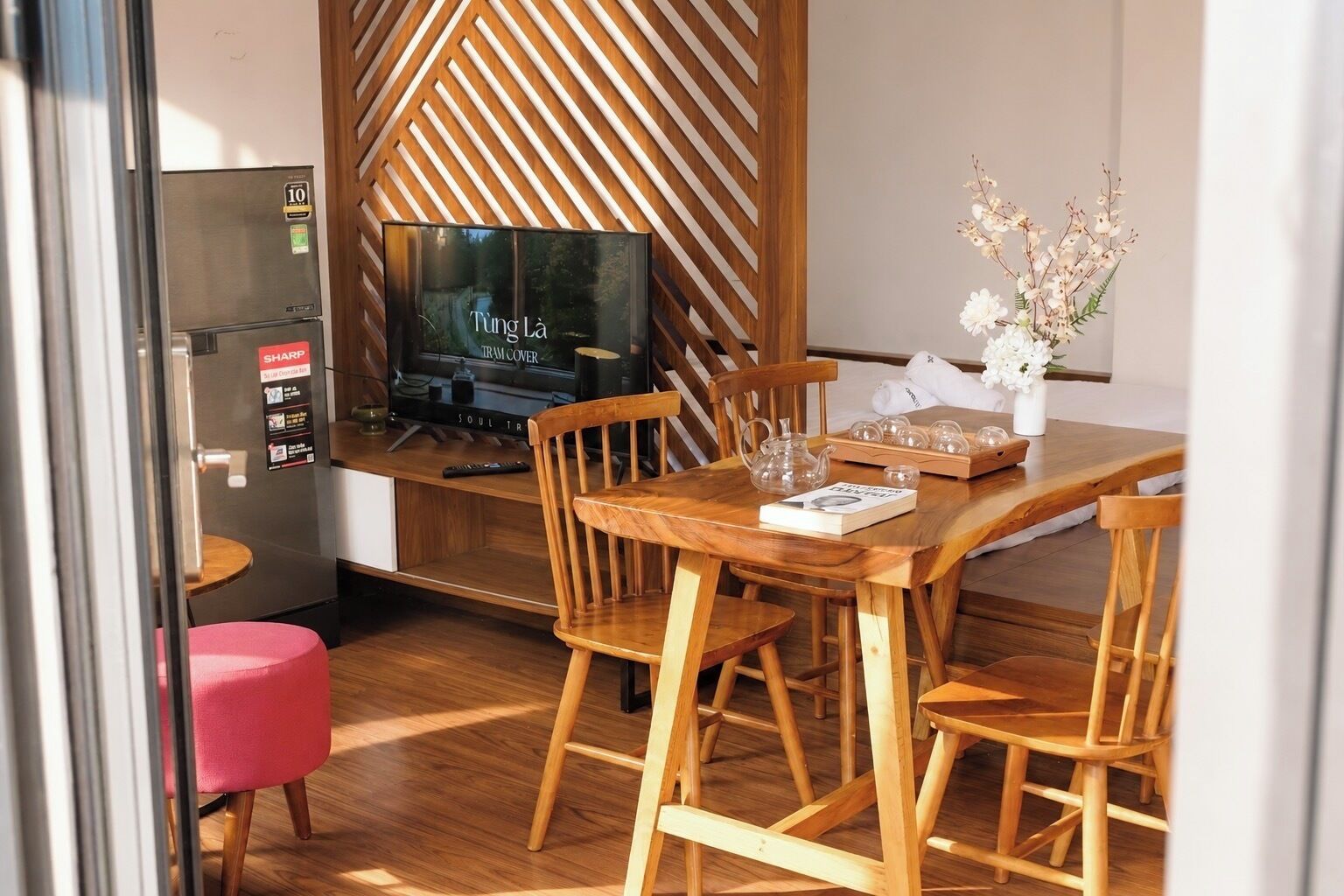 A compact living space with a wooden dining table, chairs, a television, and a small seating area with a pink chair.
