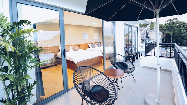 A modern hotel room with a glass wall, a balcony with outdoor seating, and a large umbrella.