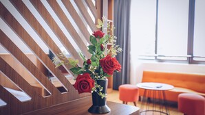 A modern room with a wooden slat wall, a vase with red roses, a round table, and an orange sofa.