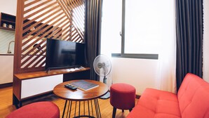 A modern hotel room with a TV, a fan, a wooden partition, and a red sofa.
