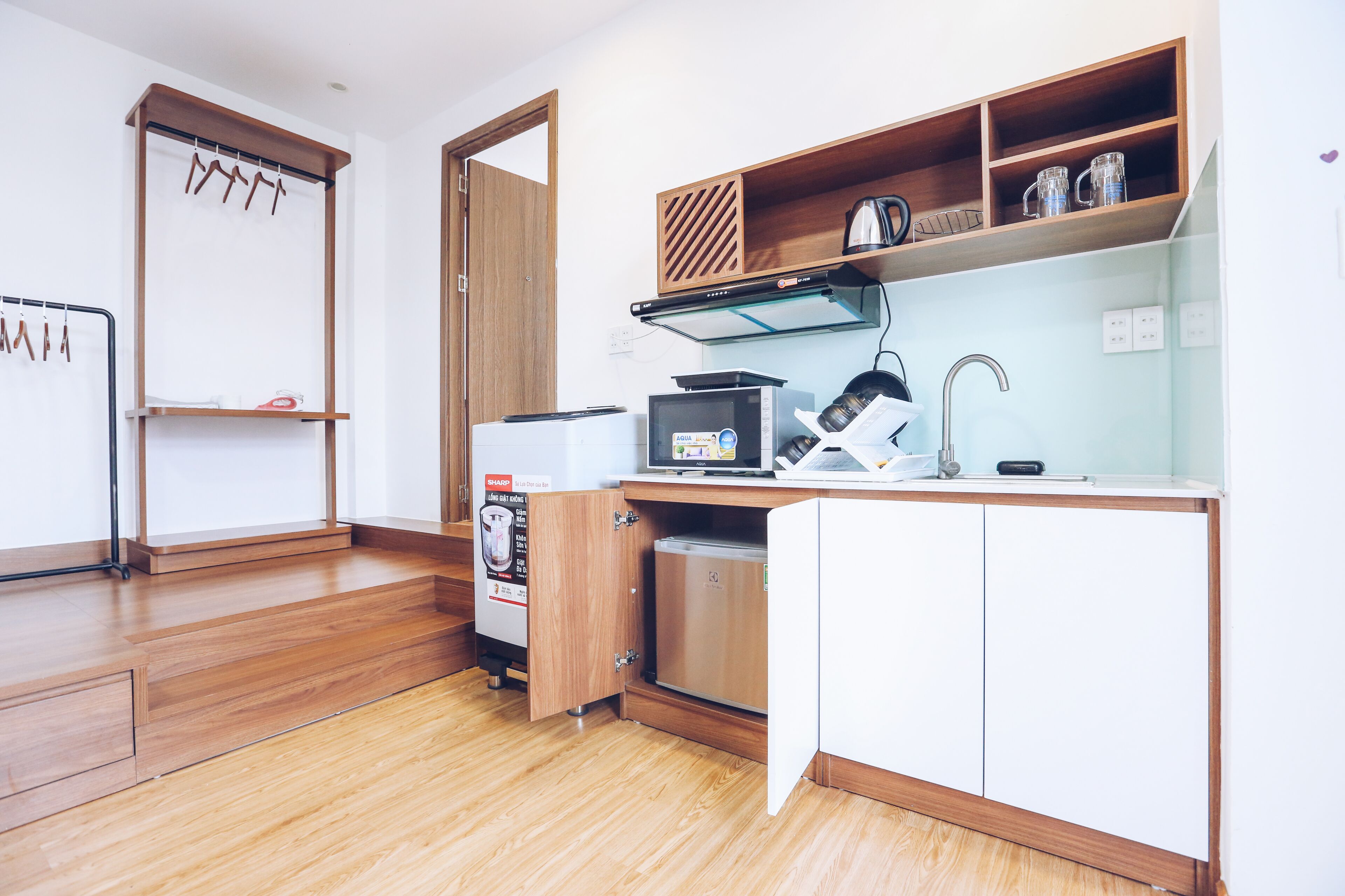 A compact kitchen with wooden cabinets, a microwave, a kettle, and a refrigerator.