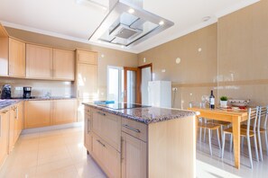 A modern kitchen with wooden cabinets, a granite countertop, a built-in oven, and a dining area with a table and chairs.