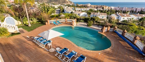 Ein Schwimmbecken mit Liegestühlen und Sonnenschirmen, umgeben von einer gefliesten Terrasse.