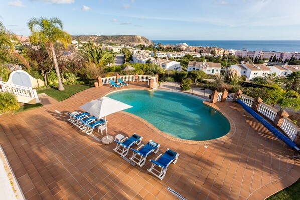 A swimming pool with lounge chairs and umbrellas, surrounded by a tiled deck.