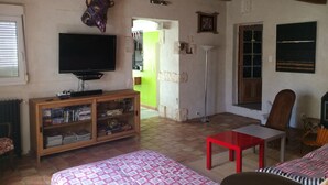 A living room with a television, bookshelf, red table, and patterned sofa. - 110m2 house + pool, No neighbors, in the countryside between Uzès and Cévennes (Occitanie)